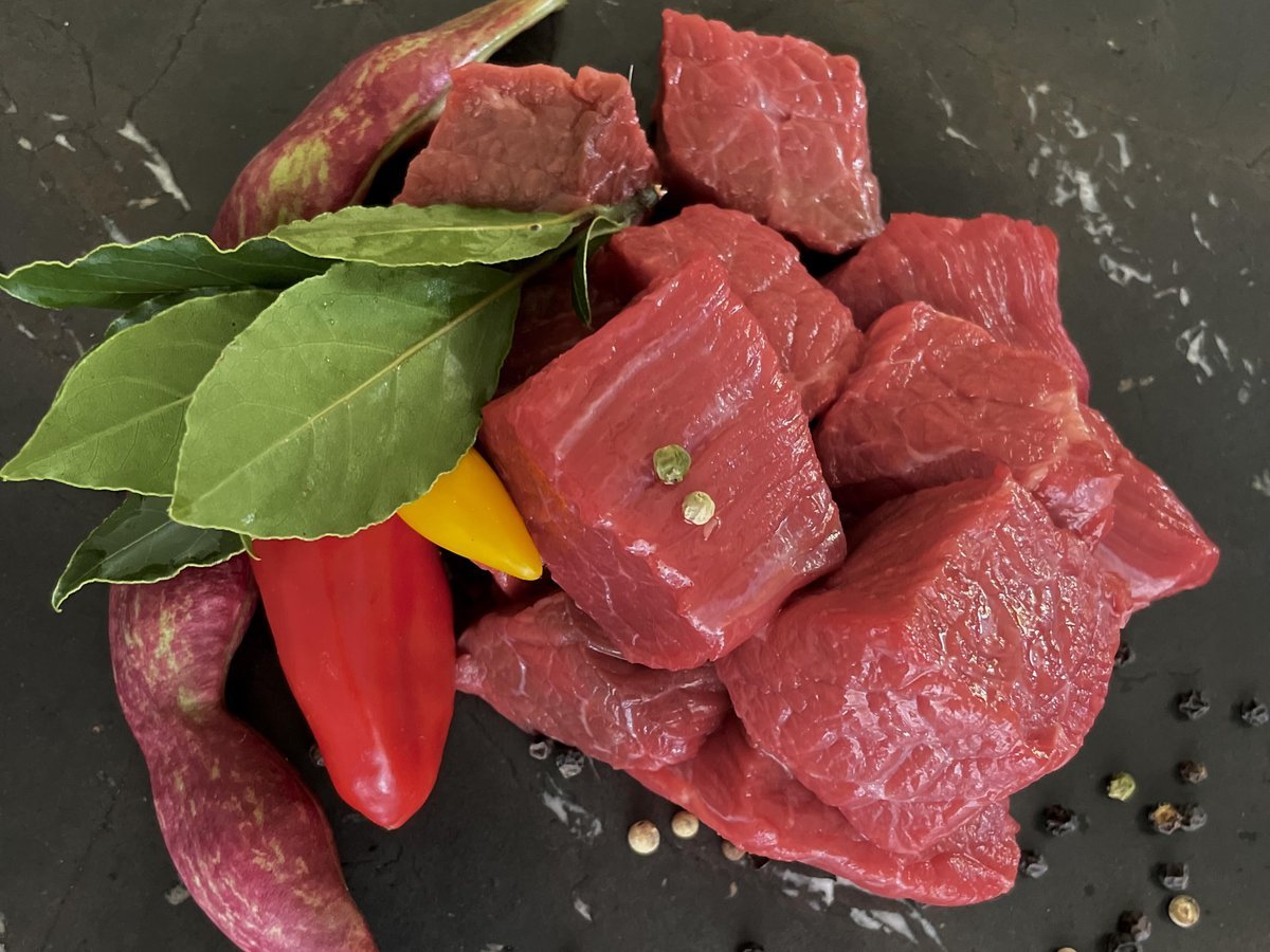 Rohe Gulaschwürfel vom Rind mit Lorbeer, Paprika und Bohnen auf dunklem Stein