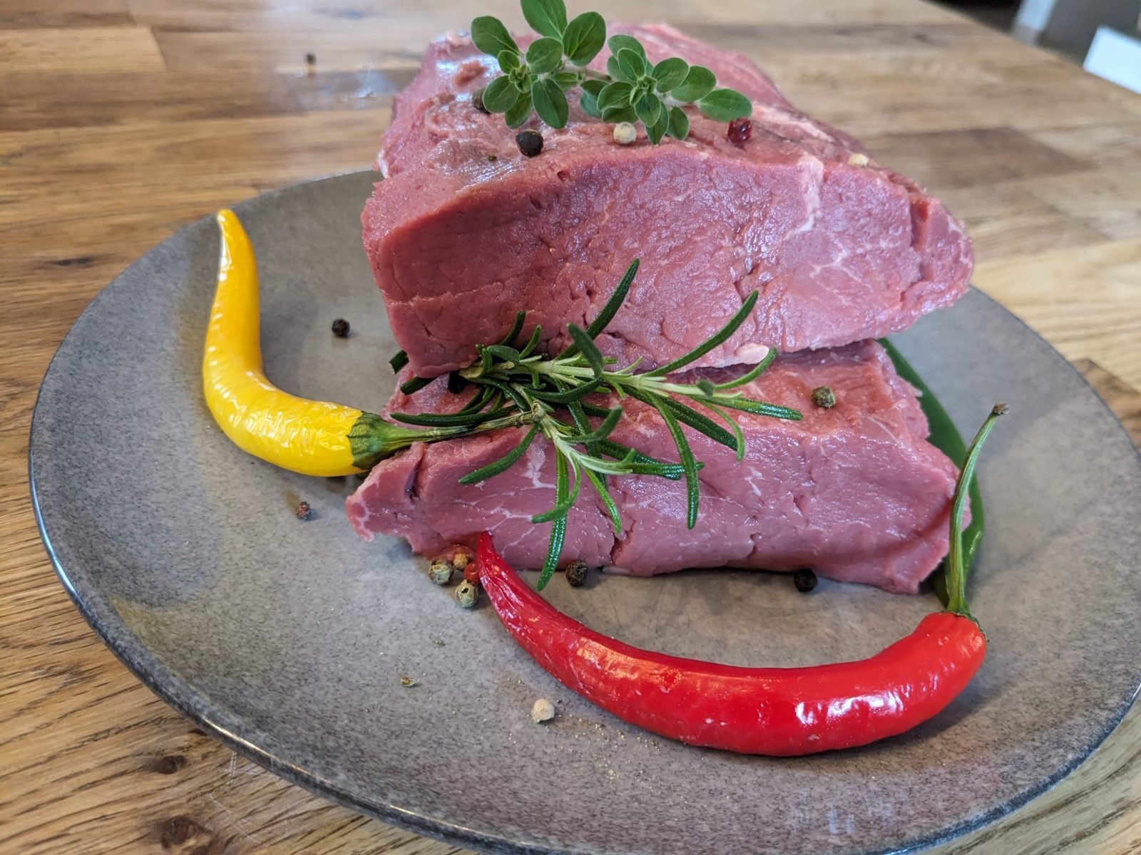 Rohes Rinderbratenstück mit Rosmarin, Thymian und Chili auf einem Teller