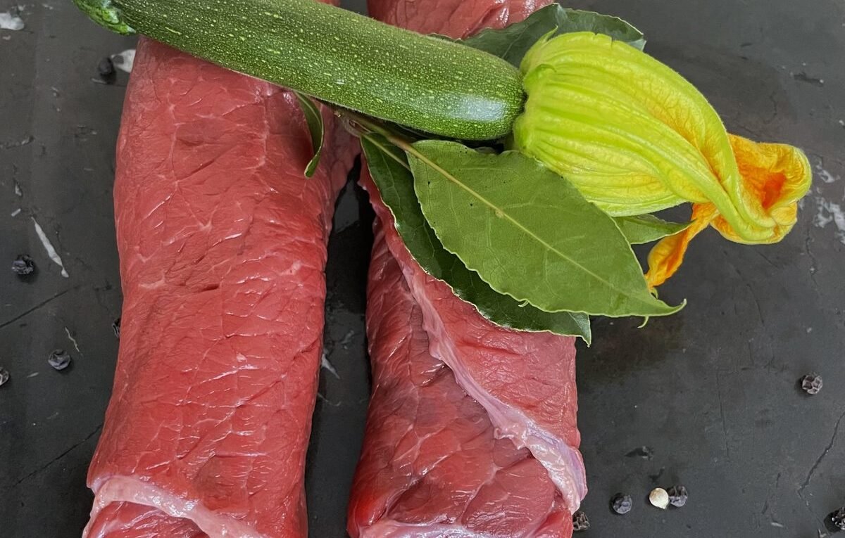 Zwei Stücke rohes Rindfleisch mit Zucchini und Lorbeer auf dunklem Stein