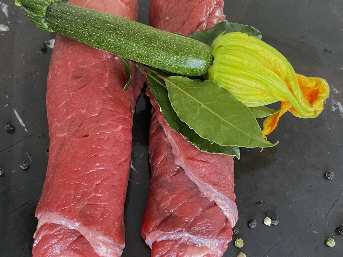 Zwei Stücke rohes Rindfleisch mit Zucchini und Lorbeer auf dunklem Stein